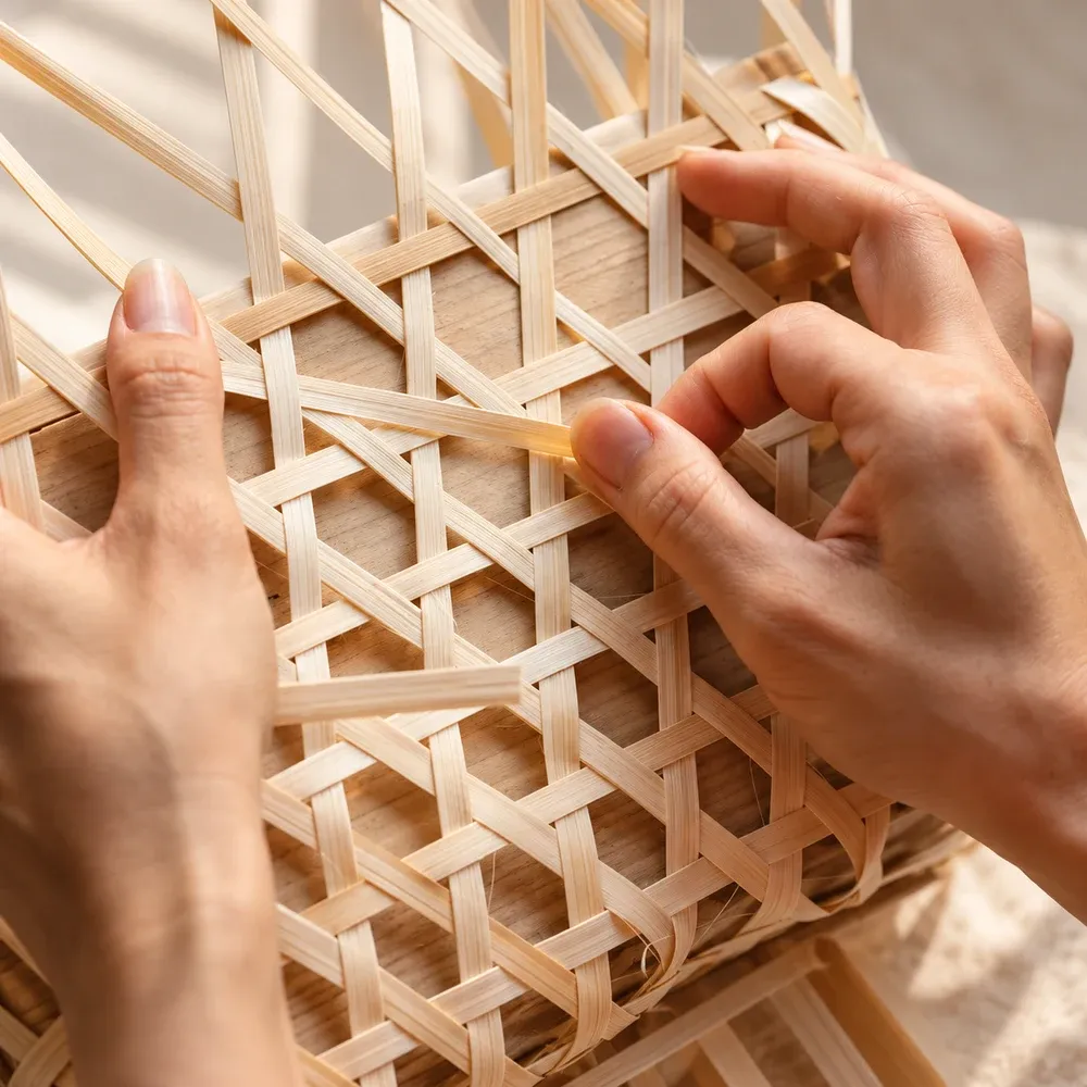 Close-up of hands interlacing narrow bamboo strips into a woven panel.